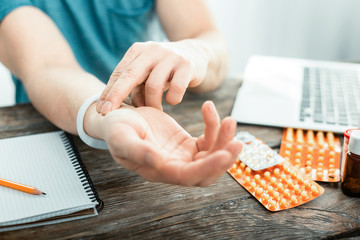 Touch and count. Sick occupied careful man sitting by the table measuring his pulse touching hand.