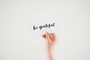 cropped shot of woman holding paper with be grateful lettering isolated on white