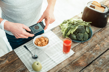 Dont forget. Concentrated attentive careful man standing near the table holding a smartphone and making photo of his food.