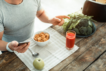 Healthy breakfast. Calm attentive smart man sitting by the table holding the cellphone and making choice what to eat.