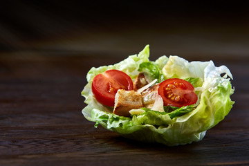 Yummy top view composition of fresh healthy salad served in lettuce leaves on wooden table.