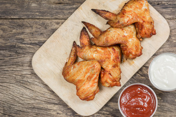 homemade style grilled chicken wings served with ketchup and mayonnaise on old wooden background, top view.