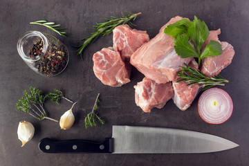 Fresh raw meat with herbs, spices and a butcher knife lies on the surface of a dark stone. Cooking concept.