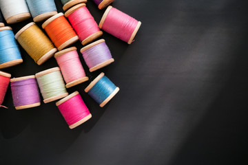 Sewing box Many multicolored sewing threads on wooden coils are scattered on a black surface