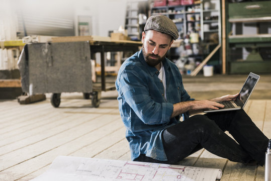 Man with laptop sitting on the floor looking at construction plan