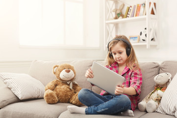 Little girl in headphones with tablet at home