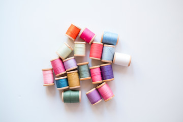 Fototapeta na wymiar Many multicolored sewing threads on wooden coils are scattered on a white surface