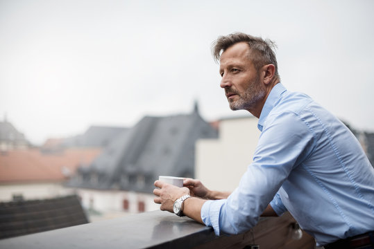 Portrait of mature businessman with cup of coffee on roof terrace