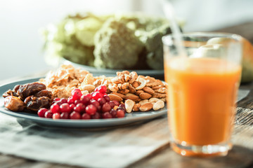 Necessary products. Helpful healthy nuts and berries being in the plate on the table near a glass of juice.