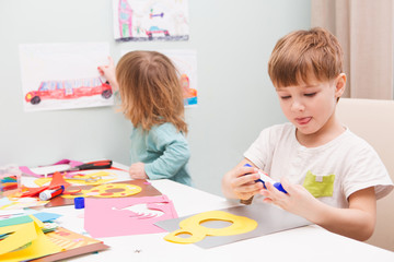 Happy cheerful children drawing  in paper using a lot of painting tools sitting at a table.   