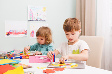 Fototapeta premium Happy cheerful children drawing in paper using a lot of painting tools sitting at a table. 