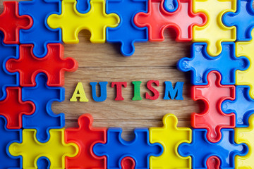 Pieces from a colorful jigsaw puzzle arranged to form a page on wooden background. Break barriers together for autism concept