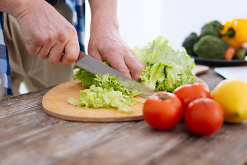 Nutrition source. Young male attractive hands using knife while preparing salad and pressing cabbage again surface