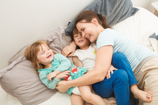 mother with her little children, son and daughter, relaxing and playing in the bed at the weekend together, lazy morning. 