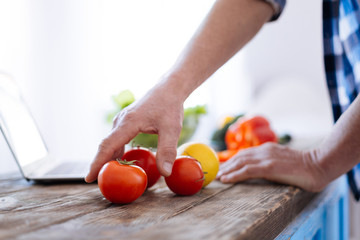 Right nutrition. Close up of attractive handsome male hands reaching for tomato for trying biohacking diet and cooking lunch