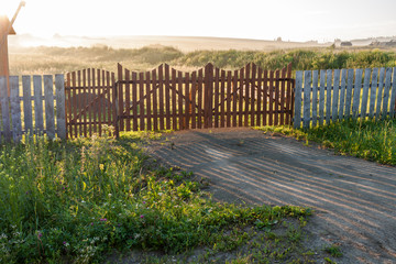 Drenched by dawn sun village fields and wooden gates.