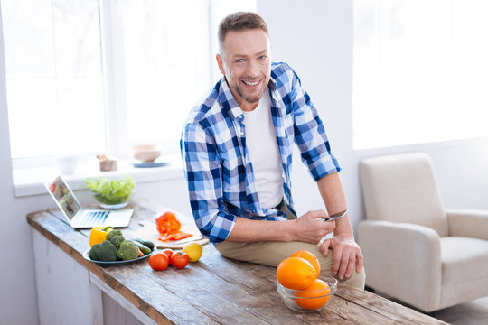 Optimize your health. Attractive cheerful bearded man looking at camera while grinning and carrying smartphone