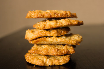 Pile of golden brown homemade oatmeal cookies on dark table background. High tower of tasty peanut oatcakes, healthy sweet home-baked products