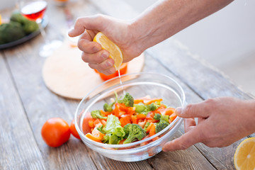 Plan ration. Selective focus of juicy bitter lemon hold by male hand while glass bowl standing on surface and filled with vegetables