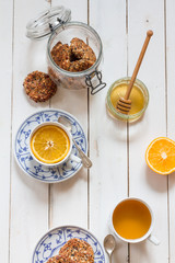 Dates and coconut cookies. Green tea with orange in white and blue cup. White wooden plate. Flatlay.