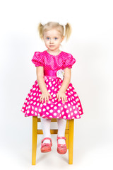 Little girl 3 years old in a red dress with bows in her hair. Beautiful girl in a beautiful fluffy dress posing against a white wall.
