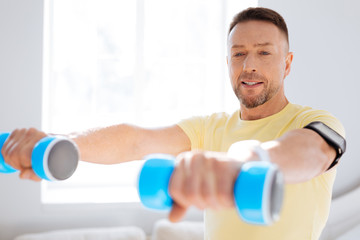 Change your habits. Attractive handsome concentrated man exercising with dumbbells for training biceps and posing on the light background