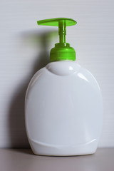 White plastic soap bottle with green dispenser for liquid soap on light beige background.