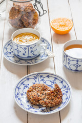 Dates and coconut cookies. Green tea with orange in white and blue cup. White wooden plate. Flatlay.