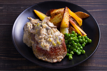 Beef steak with mushroom cream sauce, potato wedges  and green peas