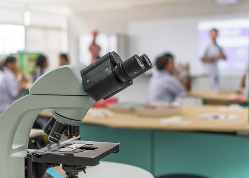Biology or chemistry science class study with microscope and blur background of school student group learning in blurry lab classroom with teacher for education concept