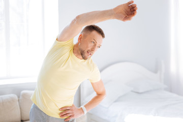 Perfect stretch. Young charming handsome man experimenting with stretching while rising hand and posing on light background