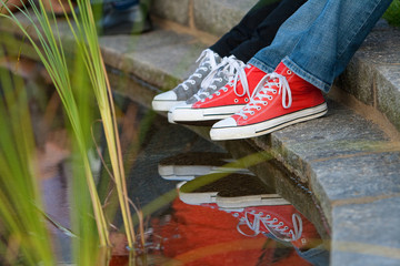 Füße und Unterschenkel zweier junger Mädchen mit bunten Turnschuhen und Jeans, die an einem...