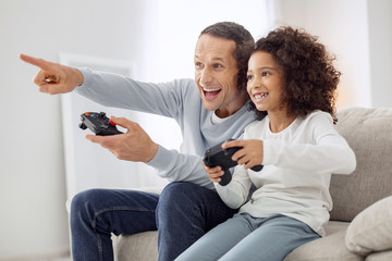 Joyful game. Pretty exuberant curly-haired girl smiling and playing games with her father while sitting on the couch