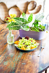 Smoke salmon dumpling salad on a white plate and on a light wooden table. Chinese food. On the table are flowers in a transparent vase and a lilac pot with green leaves. Side view with copy space. 