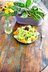 Smoke salmon dumpling salad on a white plate and on a light wooden table. Chinese food. On the table are flowers in a transparent vase and a lilac pot with green leaves. Side view with copy space. 