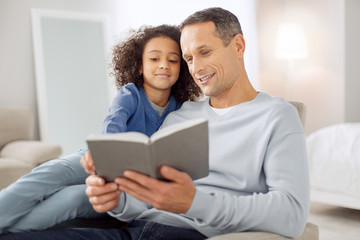 Avid readers. Attractive cheerful dark-haired reading a book and the girl sitting near him and smiling