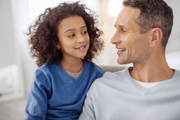 Obraz premium Happiness inside us. Attractive alert dark-haired smiling and looking at his daughter while sitting together
