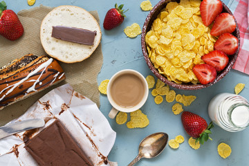 Breakfast, corn flakes with fresh strawberries and milk, chocolate butter with fresh pastries on a gray background. View from above.