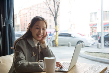 Beautiful young businesswoman smiling to the camera as she satisfied with her work sitting at the table with laptop computer, open notebook and cup of coffee.