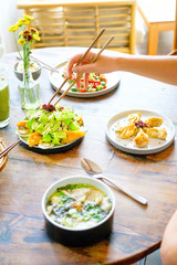 Salmon dumpling salad and Mushroom chicken Wonton soup and chicken kong pao on a white plate and on a wooden table. Chinese food. A female hand with chopsticks takes food. Side view with copy space. 