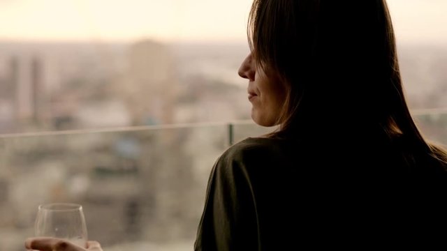 Beautiful woman drinking red wine while sitting in rooft bar in the city
