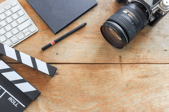 film director's desk. clapboard, book and digital camera on wood table with soft-focus and over light in the background