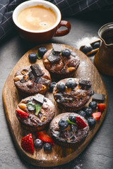 Fresh, blueberry muffins with strawberry, chocolate on a wooden board and stone background with sugar and fruits. Food background. Concept of pastry. 