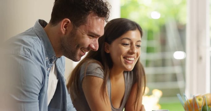 4K Smiling couple looking at laptop at home, reacting to what they see on screen