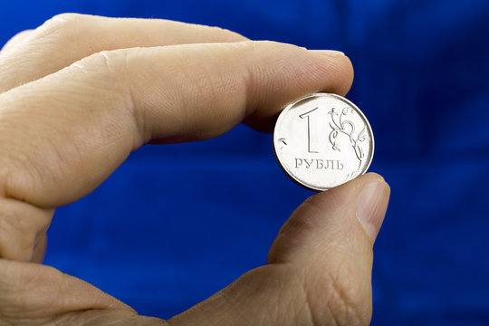 Close up of one ruble coin in the man's hand on the dark blue background