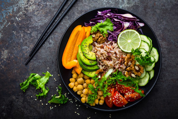 Buddha bowl dish with brown rice, avocado, pepper, tomato, cucumber, red cabbage, chickpea, fresh lettuce salad and walnuts. Healthy vegetarian eating, super food. Top view