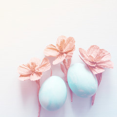 Easter eggs and decorative paper flowers on light background, top view, copy space
