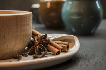 Indian tradition milk drink, masala chai tea with spices. Close up Wooden cup on ceramic plate, Cinnamon Stick, Clove, Star Anise,