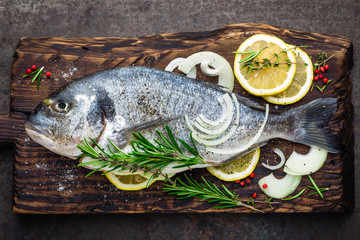 Fresh fish dorado with ingredients for cooking on wooden board. Raw sea bream or dorada fish on dark vintage metal background. Dietary food. Top view