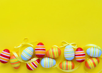 Colorful easter eggs and ribbons on a yellow background with empty space. Top view
